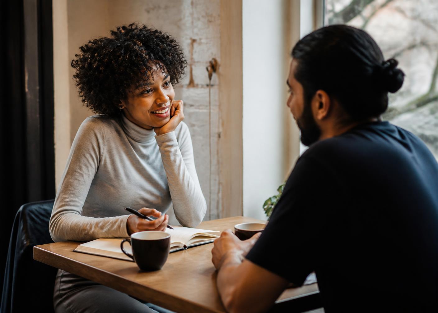 Two people having a relaxed conversation over coffee with a notebook open